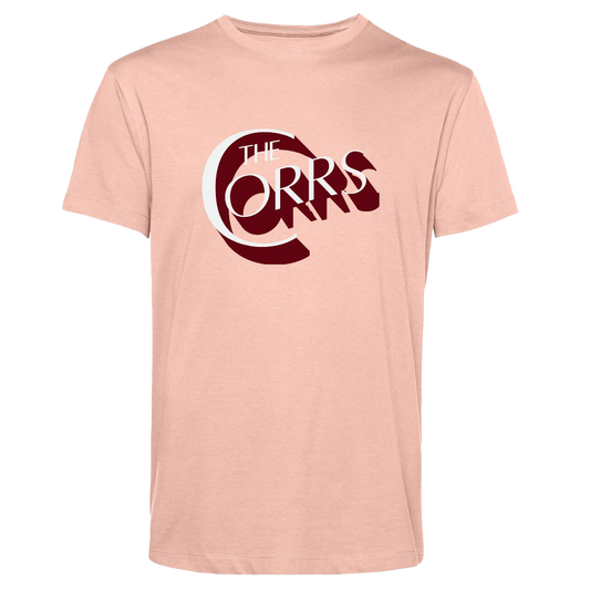 The Corrs Serif Soft Rose T-Shirt from The Corrs Store by National Merchandise is a light pink, organic tee with bold dark red and white The Corrs text on soft 145gsm fabric, shown on a bright green background.