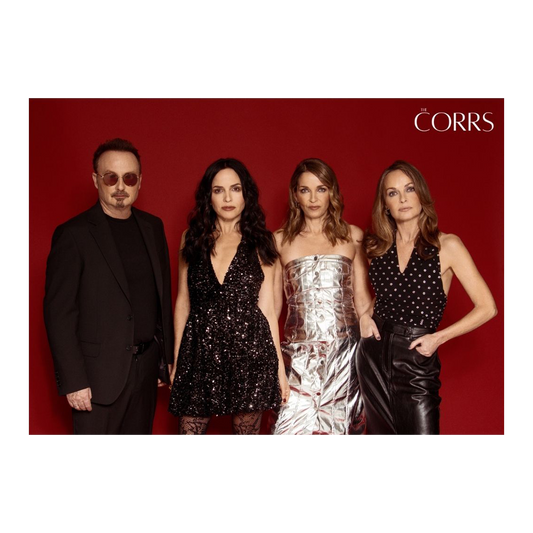 An A3 poster from The Corrs Store by National Merchandise features four people against a red background, with a man in dark sunglasses and black suit, three women in stylish black or metallic outfits, and THE CORRS in white at the top right.